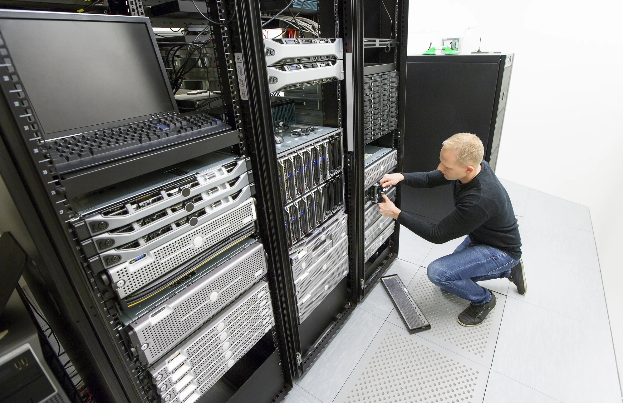 Un technicien informatique travaille dans une salle de serveurs, agenouillé devant des baies de serveurs ouvertes